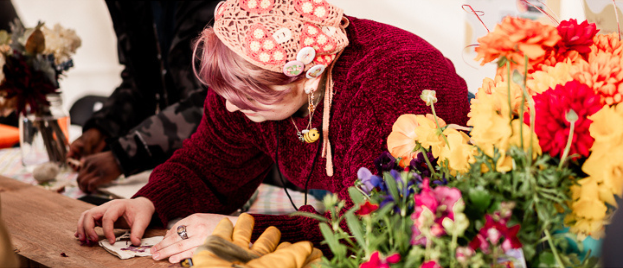 Person engaged in a craft project at a table with vibrant flowers in the foreground.