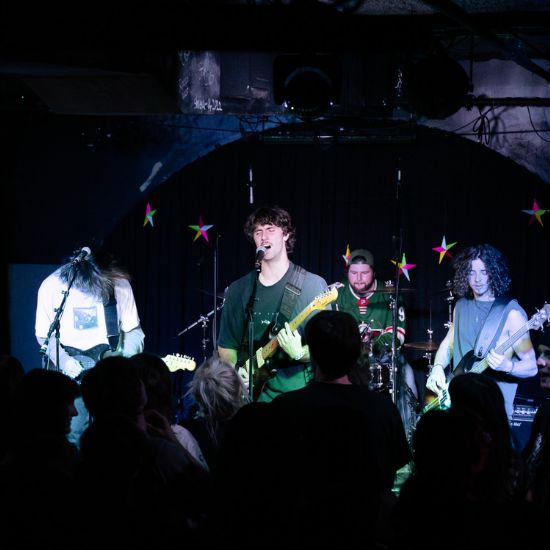 A band performing on stage with electric guitars, a guitarist singing, a bassist, and a drummer.